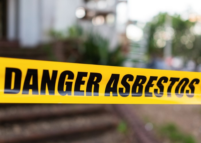 Yellow danger asbestos warning tape across a blurred building exterior